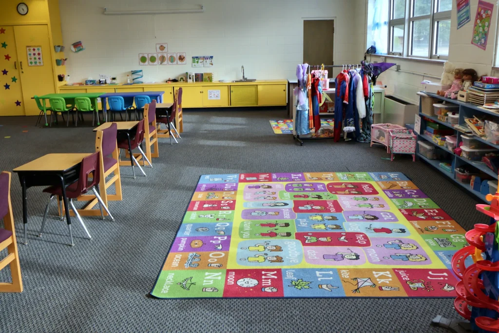 Wide view of a Hand in Hand ABA classroom with an alphabet rug, dress-up rack and desks